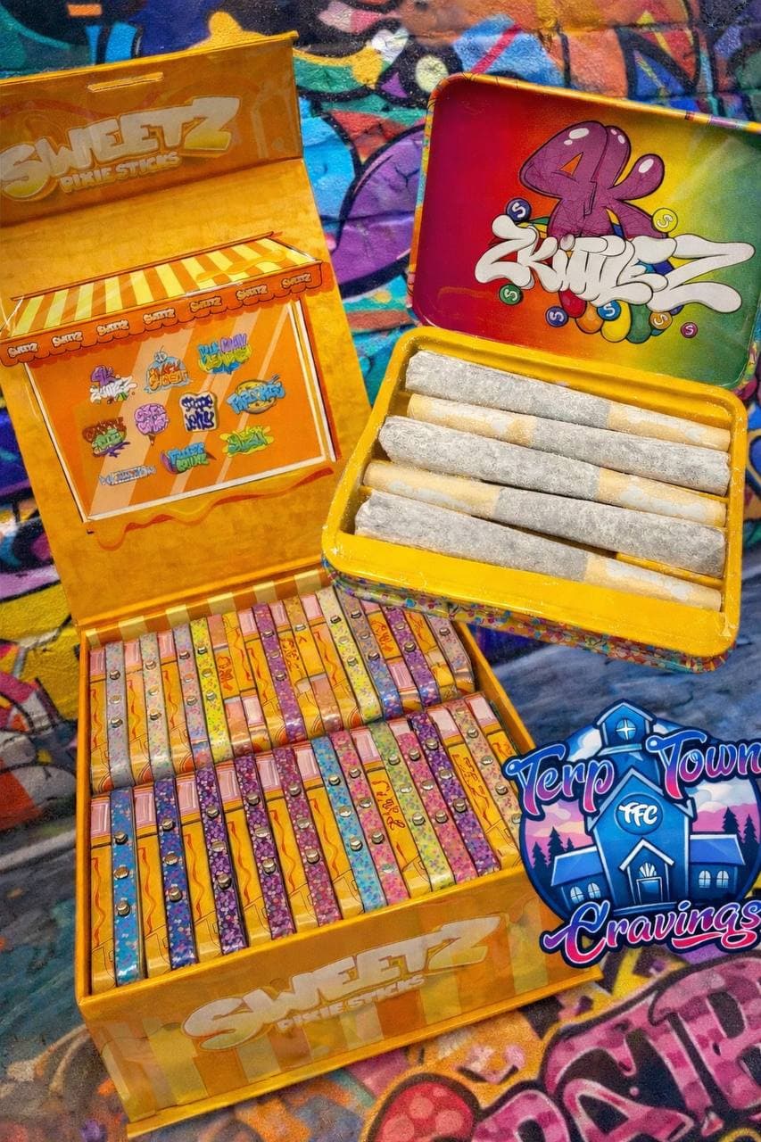 Yellow Sweetz Pixie Sticks box with colorful tins, one open revealing pre-rolled joints on graffiti.